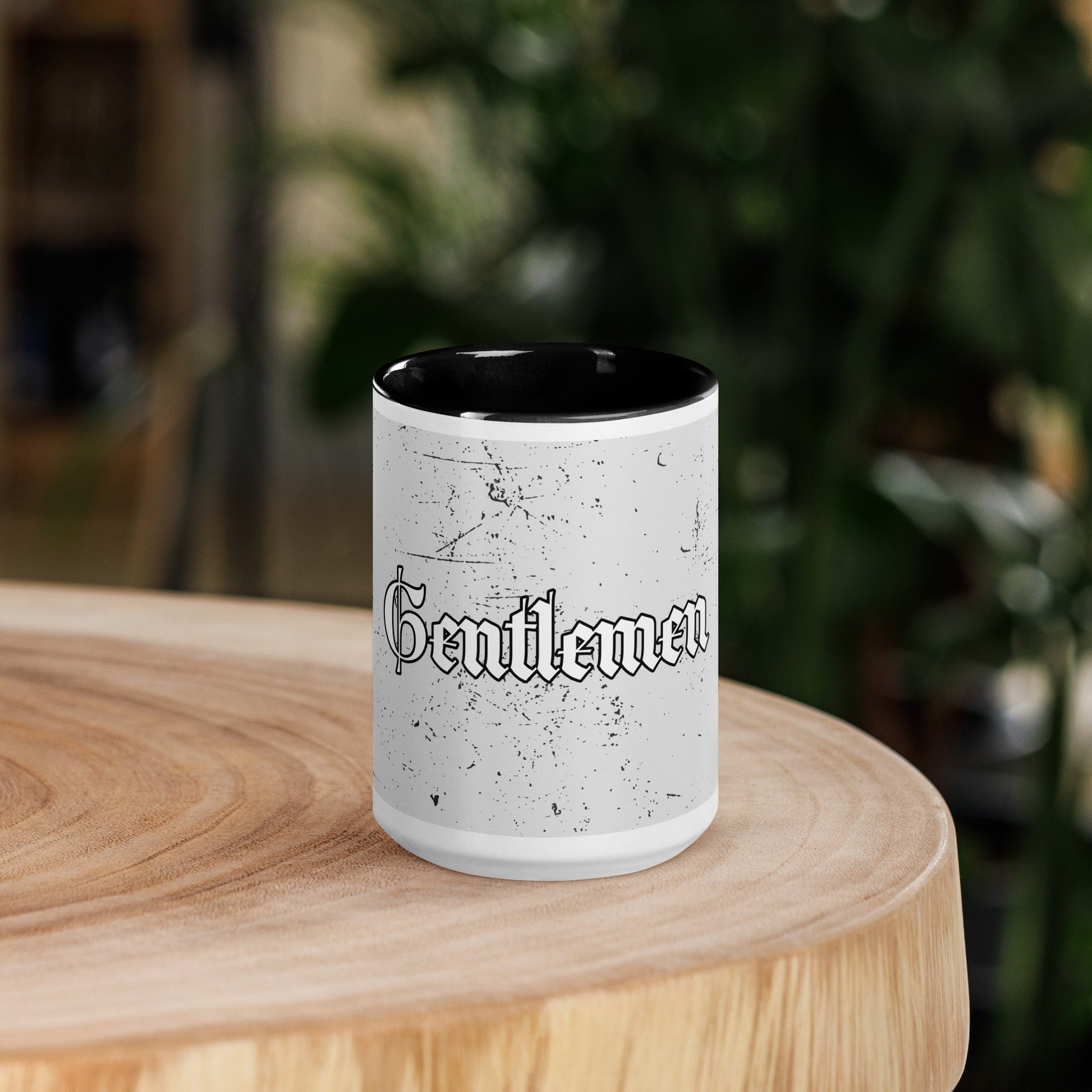 White mug with black interior on a wooden surface, featuring the word 'Gentlemen'.
